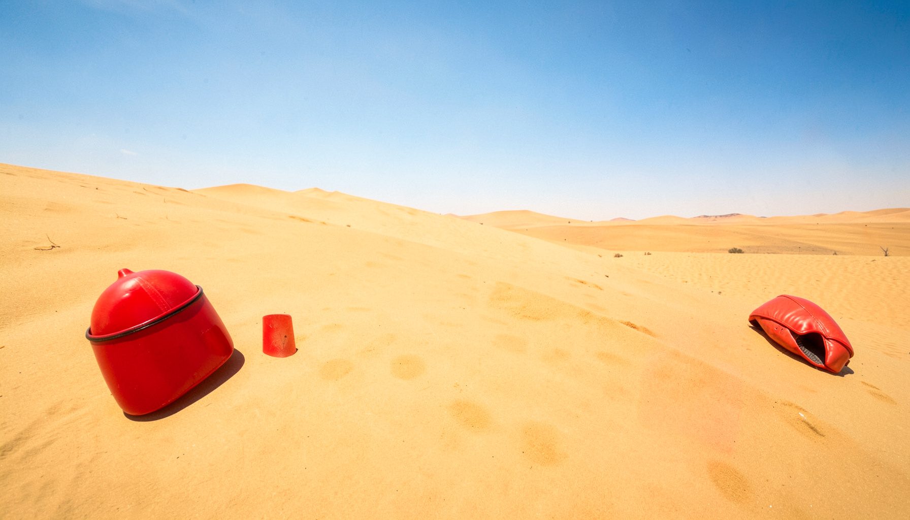 A vast desert landscape under a bright blue sky with intense sunlight flooding the terrain, warm golden and amber tones dominating the scene.